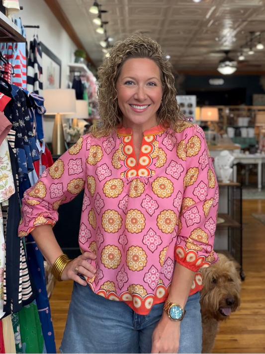 Woman in a pink patterned blouse standing in a store with a dog by her side.