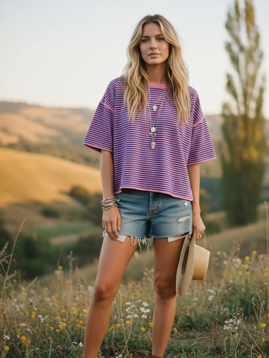 Woman in a purple shirt and denim shorts standing in a field with a scenic background