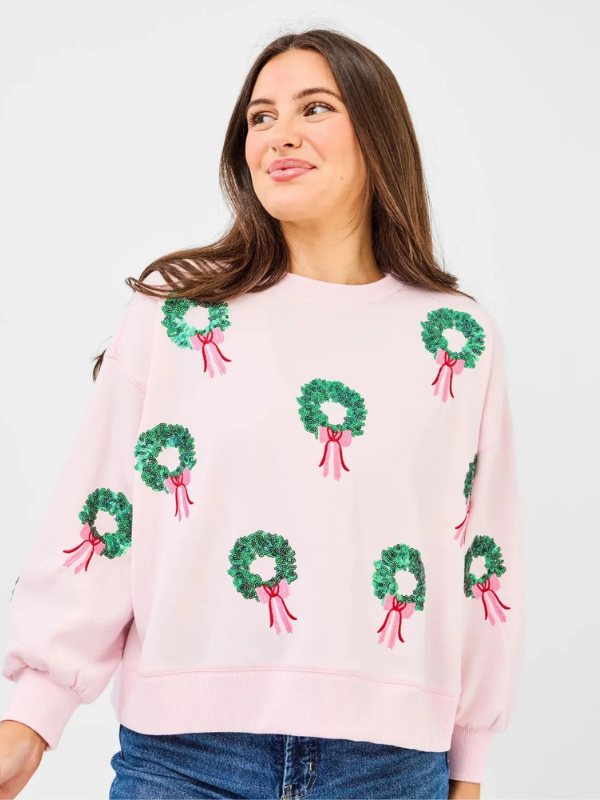 Woman wearing a pink sweater with green wreath patterns on a plain background