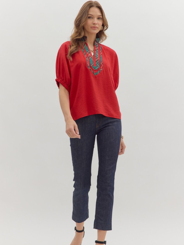 Woman wearing a red blouse with embroidery and dark jeans on a white background