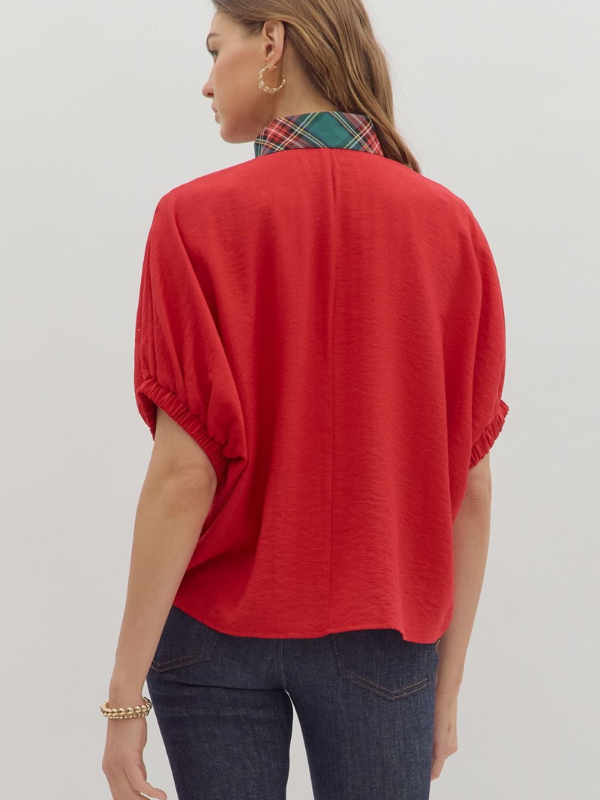 Woman wearing a red blouse with short sleeves and blue jeans on a plain background