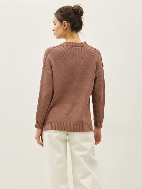 Woman wearing a brown sweater and white pants on a light background