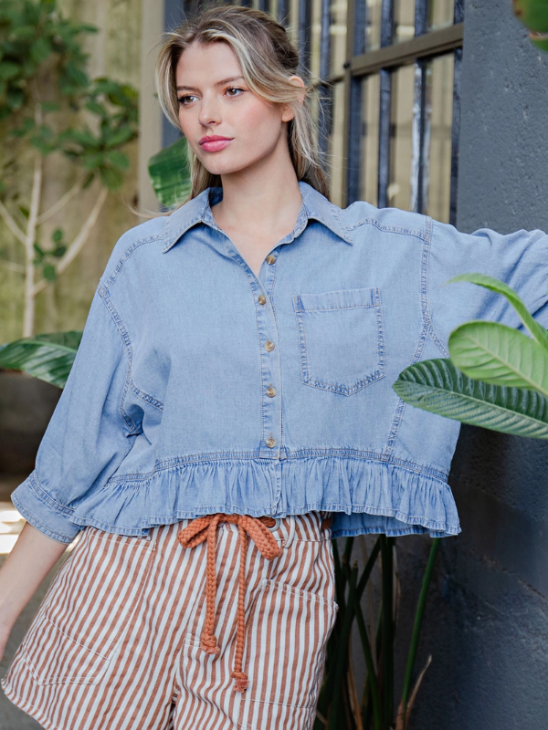 Woman wearing a light blue denim shirt with ruffled edges outdoors.