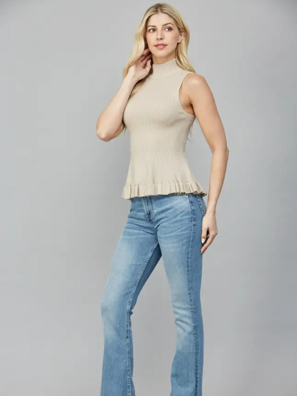 Woman wearing a beige sleeveless top and blue jeans on a gray background