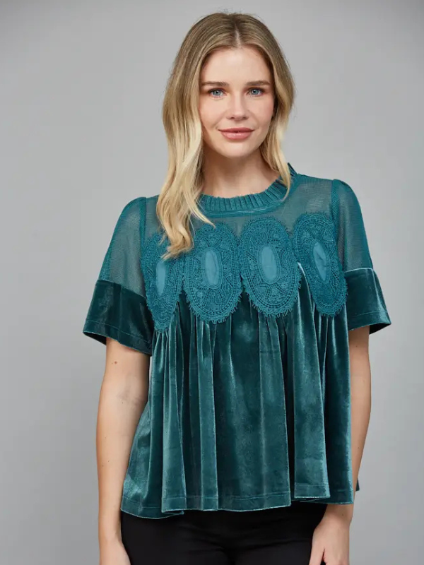 Woman wearing a teal blouse with lace details on a gray background
