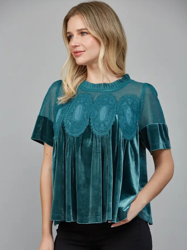 Woman wearing a teal blouse with lace details on a gray background