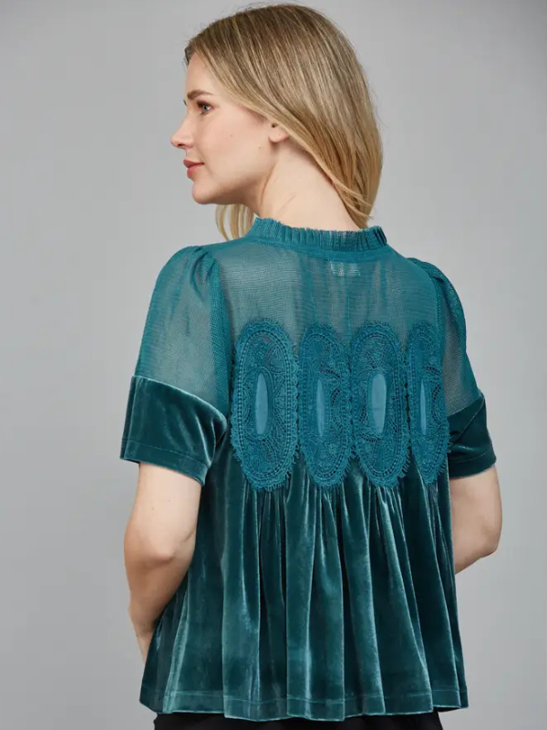 Woman wearing a teal blouse with lace detailing on a gray background