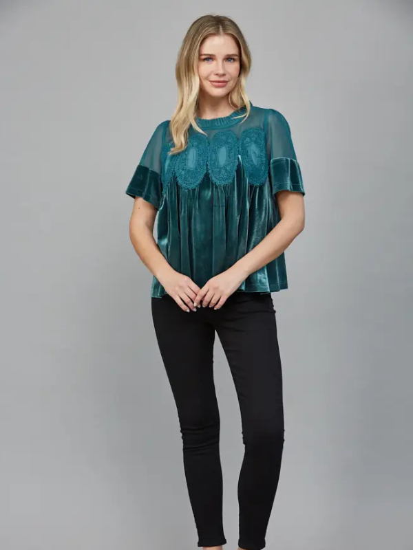 Woman wearing a teal blouse with black pants on a gray background