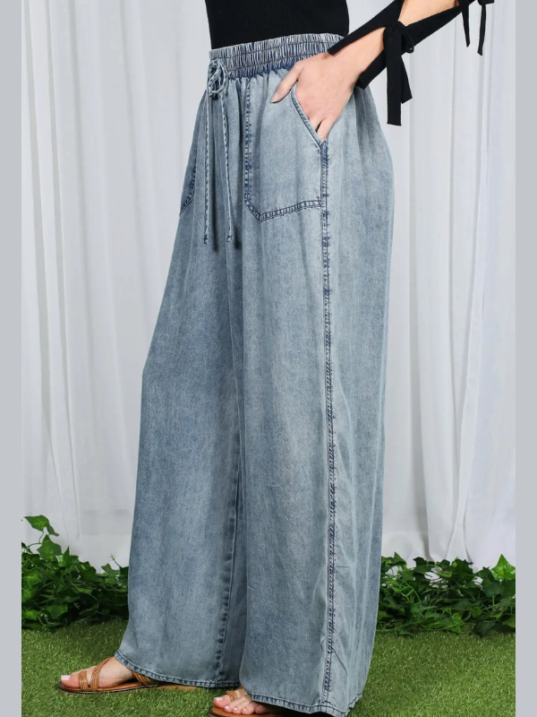 Light blue denim wide-leg pants worn by a person on a white background with greenery at the bottom.
