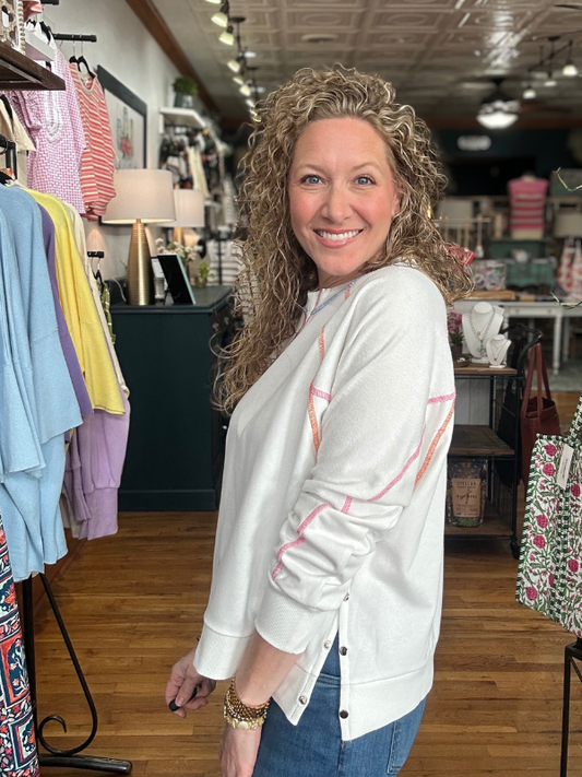 Woman wearing a white sweatshirt with colorful accents in a clothing store.