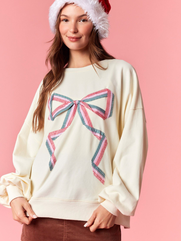 Woman wearing a cream sweater with a large bow design on a pink background