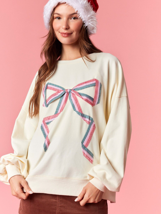 Woman wearing a cream sweater with a large bow design on a pink background