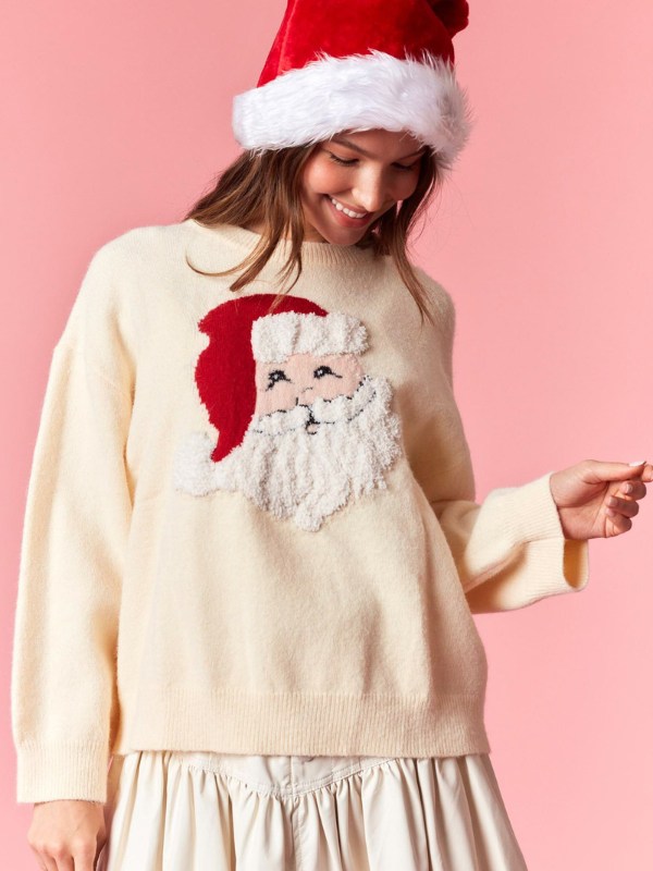 Woman wearing a cream sweater with a Santa Claus design and a red Santa hat on a pink background