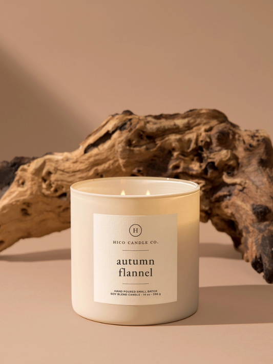 Candle labeled 'autumn flannel' from HICO CANDLE CO. on a beige background with driftwood.