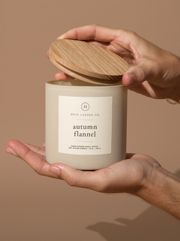 Hand holding a candle labeled 'autumn flannel' by High Candle Co. on a beige background