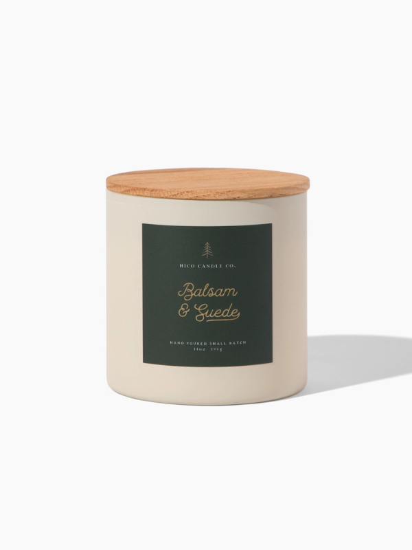 Candle with wooden lid and 'Balsam & Suede' label on a white background