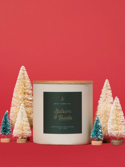 Candle with 'Balsam & Cedar' label surrounded by small Christmas trees on a red background