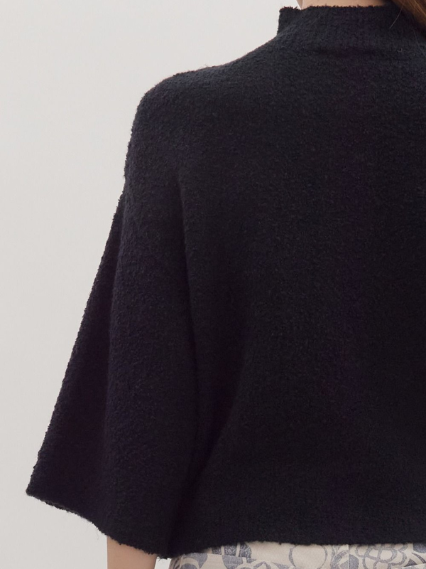 Black poncho worn by a person on a light gray background