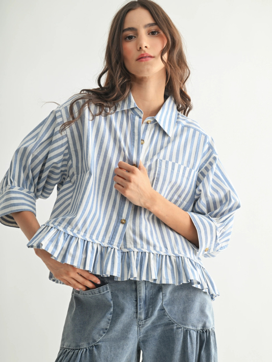 Woman wearing a blue and white striped shirt with ruffled details on a plain background