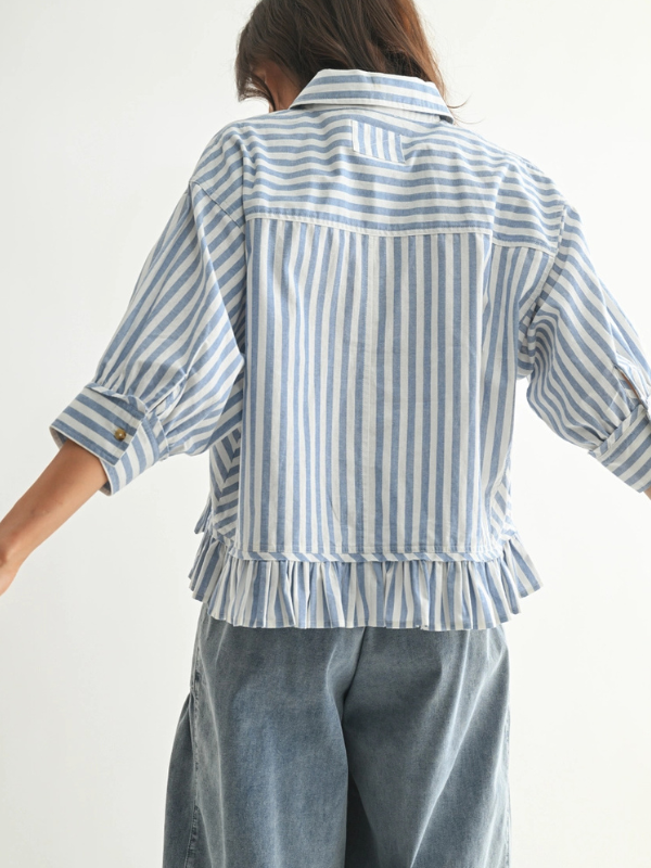 Person wearing a blue and white striped shirt with ruffled sleeves on a plain background