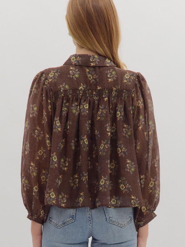 Person wearing a brown floral blouse with long sleeves on a plain background