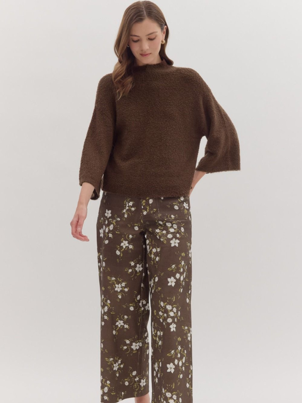 Woman wearing a brown sweater and floral pants on a white background