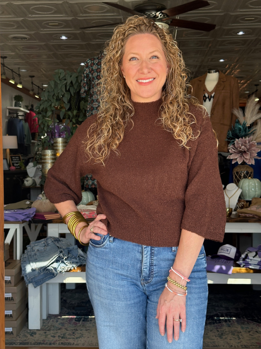 Woman wearing a brown sweater and blue jeans in a store setting