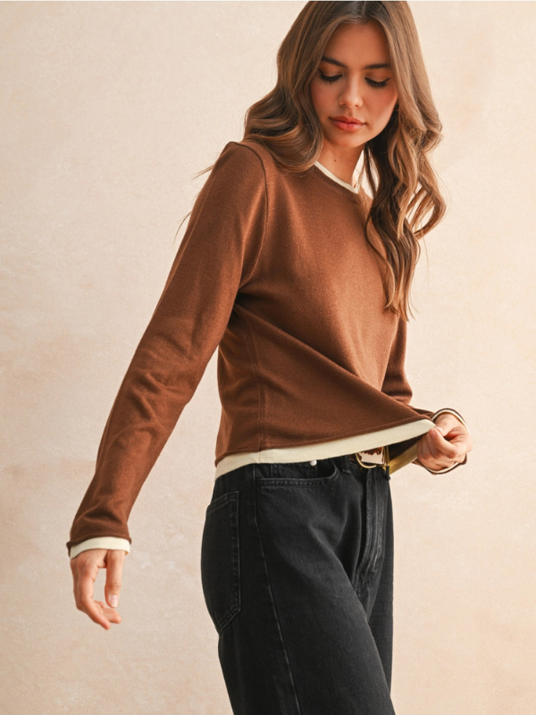 Woman wearing a brown sweater and dark pants against a beige background