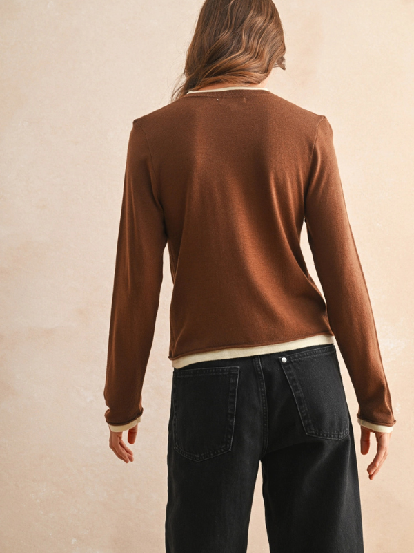 Person wearing a brown sweater and dark jeans against a beige background