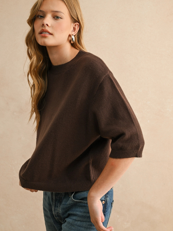 Woman wearing a brown sweater and blue jeans against a beige background