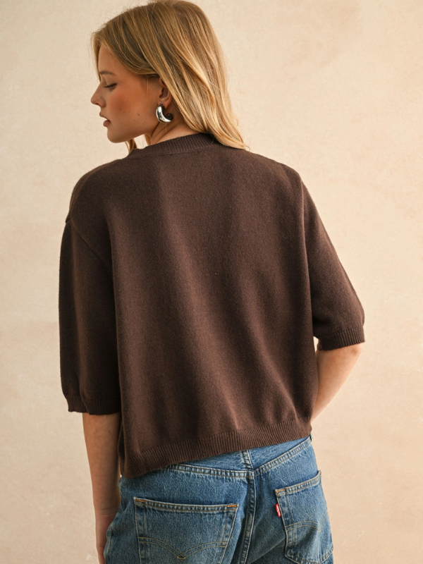 Person wearing a brown sweater and blue jeans against a beige background