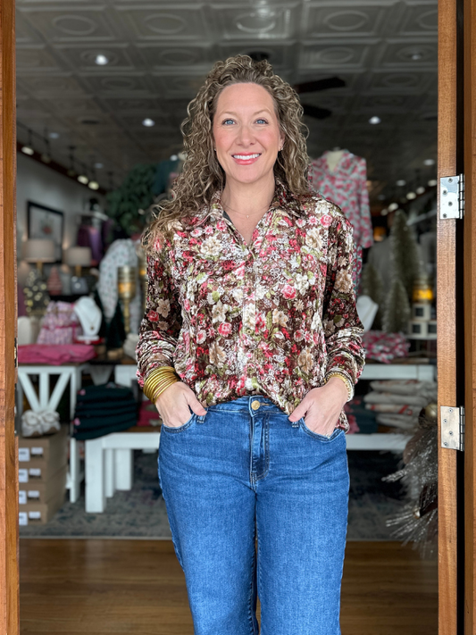 Woman wearing a floral blouse and blue jeans standing inside a store.