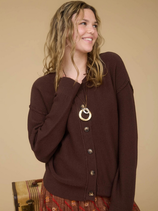 Woman wearing a brown cardigan with a necklace against a beige background