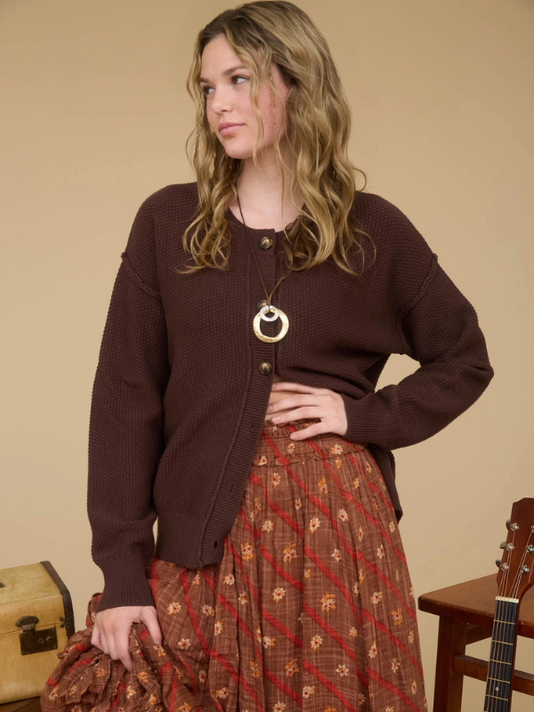Woman wearing a brown cardigan and patterned skirt with a beige background