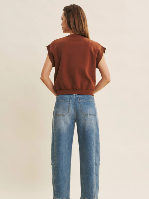 Woman wearing a rust-colored top and blue jeans on a beige background