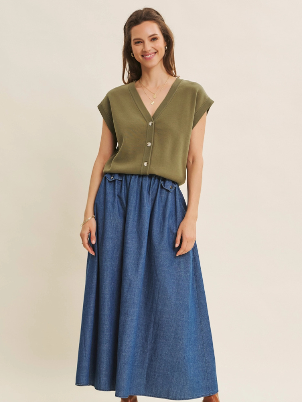 Woman wearing an olive green top and blue denim skirt on a beige background