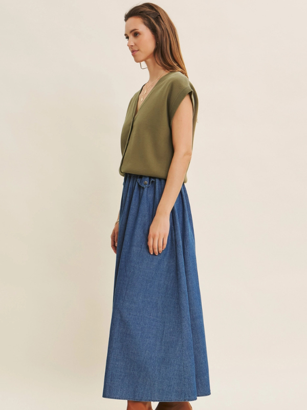 Woman wearing an olive green top and blue denim skirt on a beige background