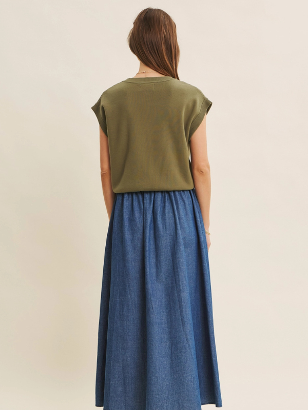 Woman wearing an olive green top and blue denim skirt on a beige background