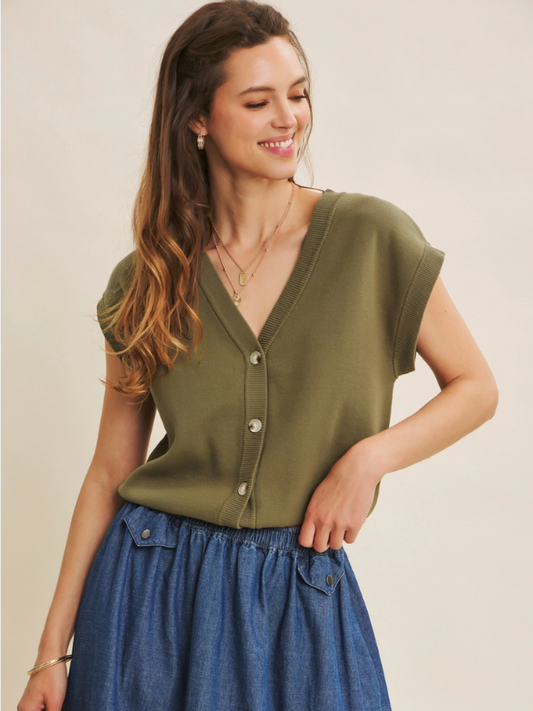 Woman wearing an olive green top and blue skirt against a beige background