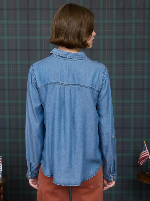 Person wearing a blue denim shirt in front of a plaid wall.