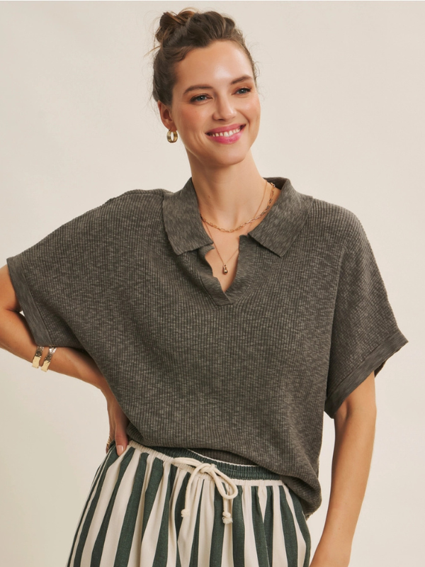 Woman wearing a dark green short-sleeve top with a collar and striped pants on a beige background