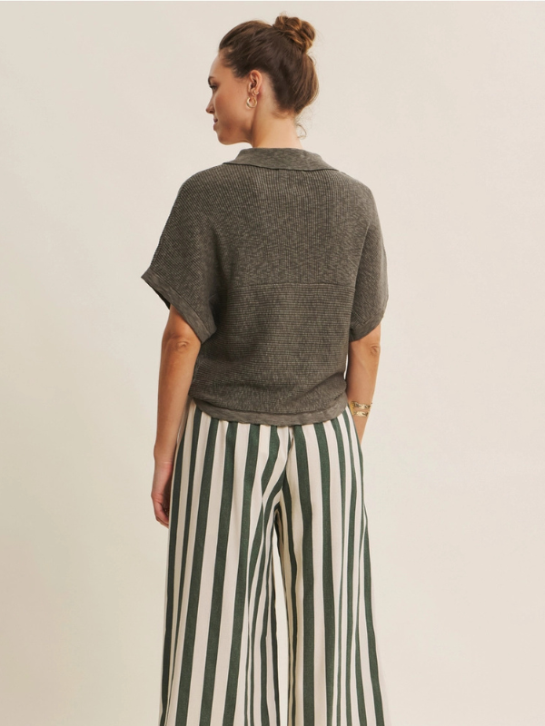 Woman wearing a gray sweater and green and white striped pants on a beige background