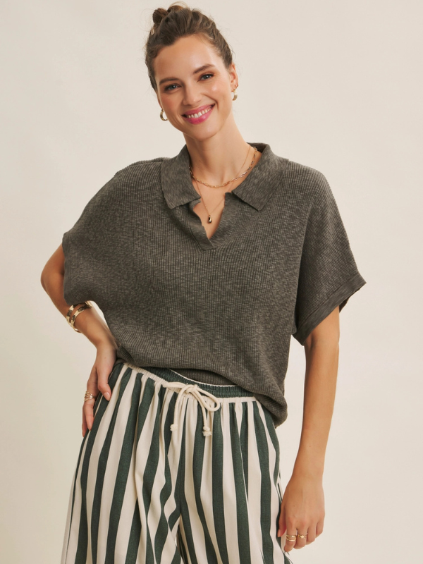 Woman wearing a gray knit top and striped pants against a plain background