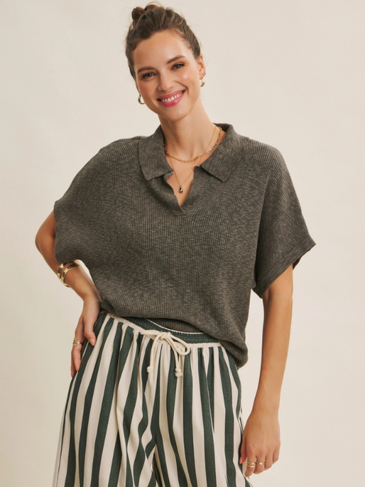 Woman wearing a gray knit top and striped pants against a plain background