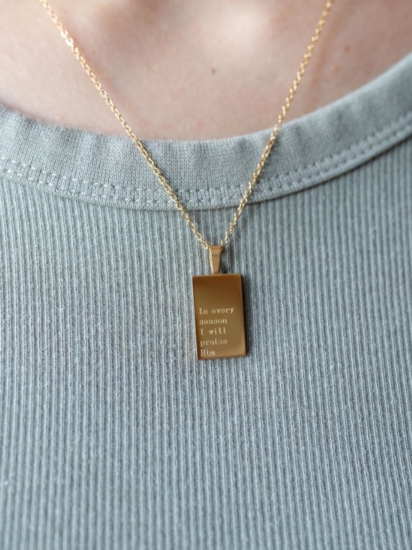 Gold necklace with a rectangular pendant on a light blue shirt