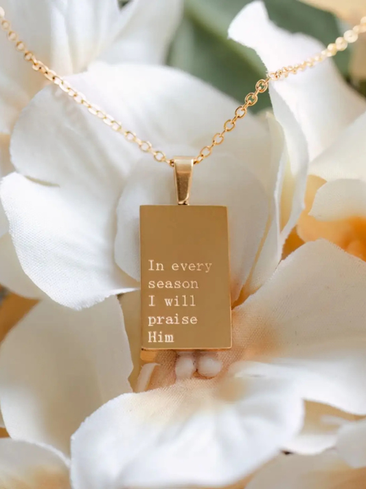 Gold necklace with a pendant featuring engraved text, set against a floral background.