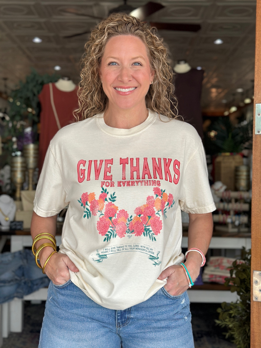 Woman wearing a 'Give Thanks for Everything' t-shirt with floral design in a store setting.