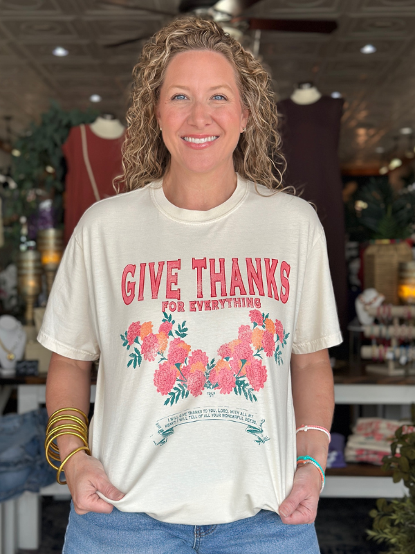 Woman wearing a 'Give Thanks for Everything' t-shirt with floral design in a store setting.