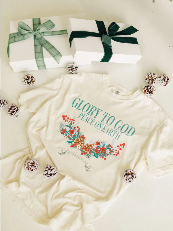 White tshirt with 'Glory to God Peace on Earth' text and floral design, surrounded by Christmas-themed items.