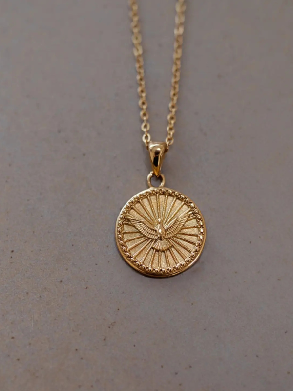Gold necklace with a circular pendant on a gray background